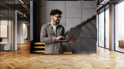 Portrait of handsome man office worker with laptop in hands standing in office Wall mural